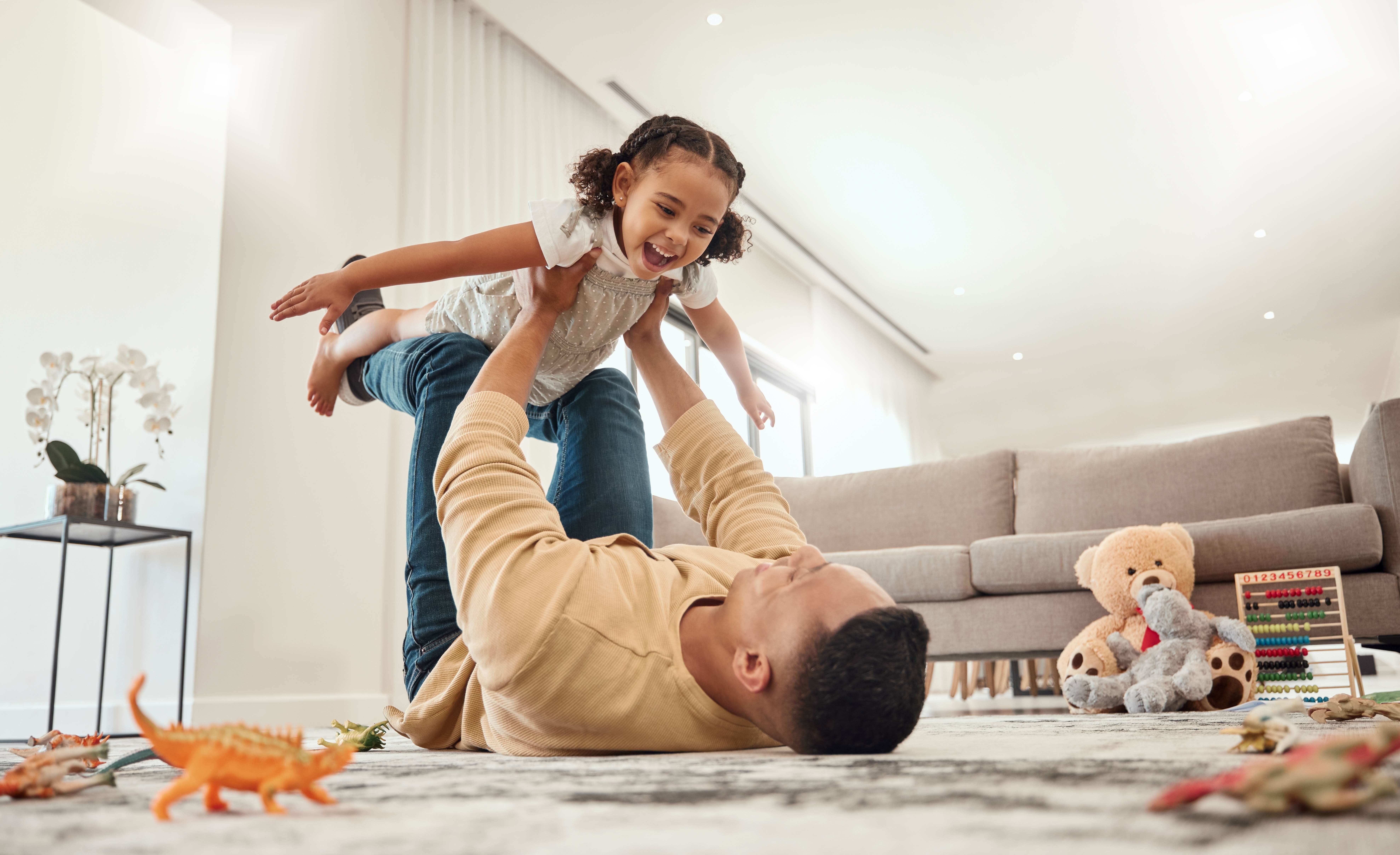 Pai brincando com sua filha no living room, uma cena de alegria e diversão, com brinquedos no chão e um ambiente acolhedor em casa.