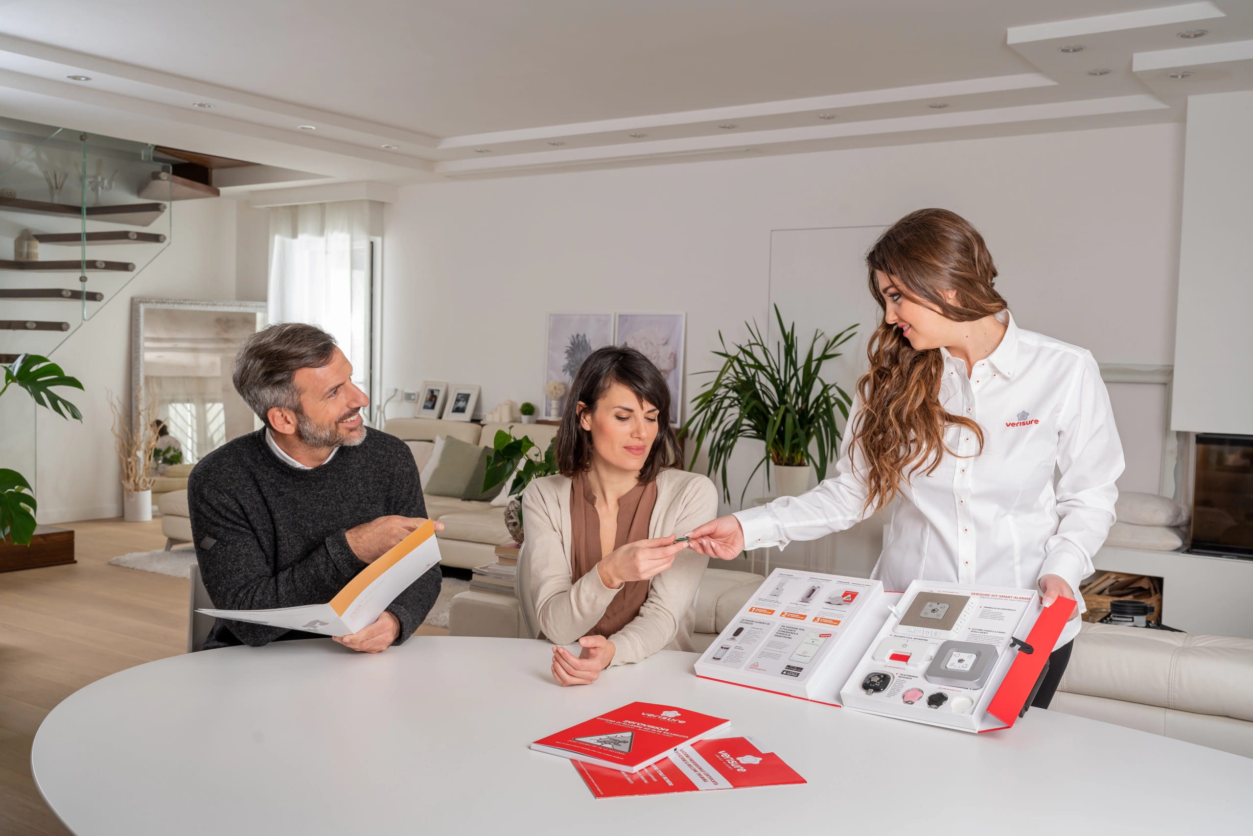 Líder de vendas Verisure apresentando catálogo de produtos para casal em reunião de negócios.