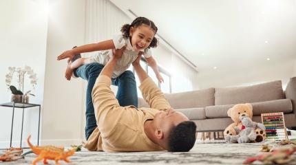 Pai brincando com sua filha no living room, uma cena de alegria e diversão, com brinquedos no chão e um ambiente acolhedor em casa.