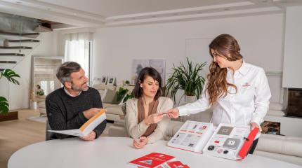 Líder de vendas Verisure apresentando catálogo de produtos para casal em reunião de negócios.
